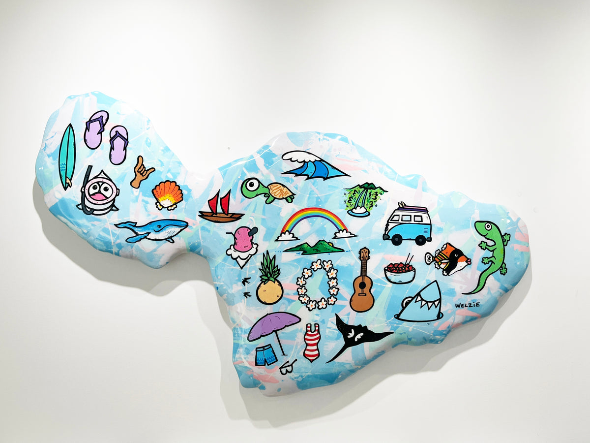A whimsical, hand-painted rock wall sculpture shaped like a tropical beach map, decorated with colorful cartoon illustrations of surfboards, flip-flops, a turtle, a rainbow, a van, and a lizard, mounted on a plain white wall.
