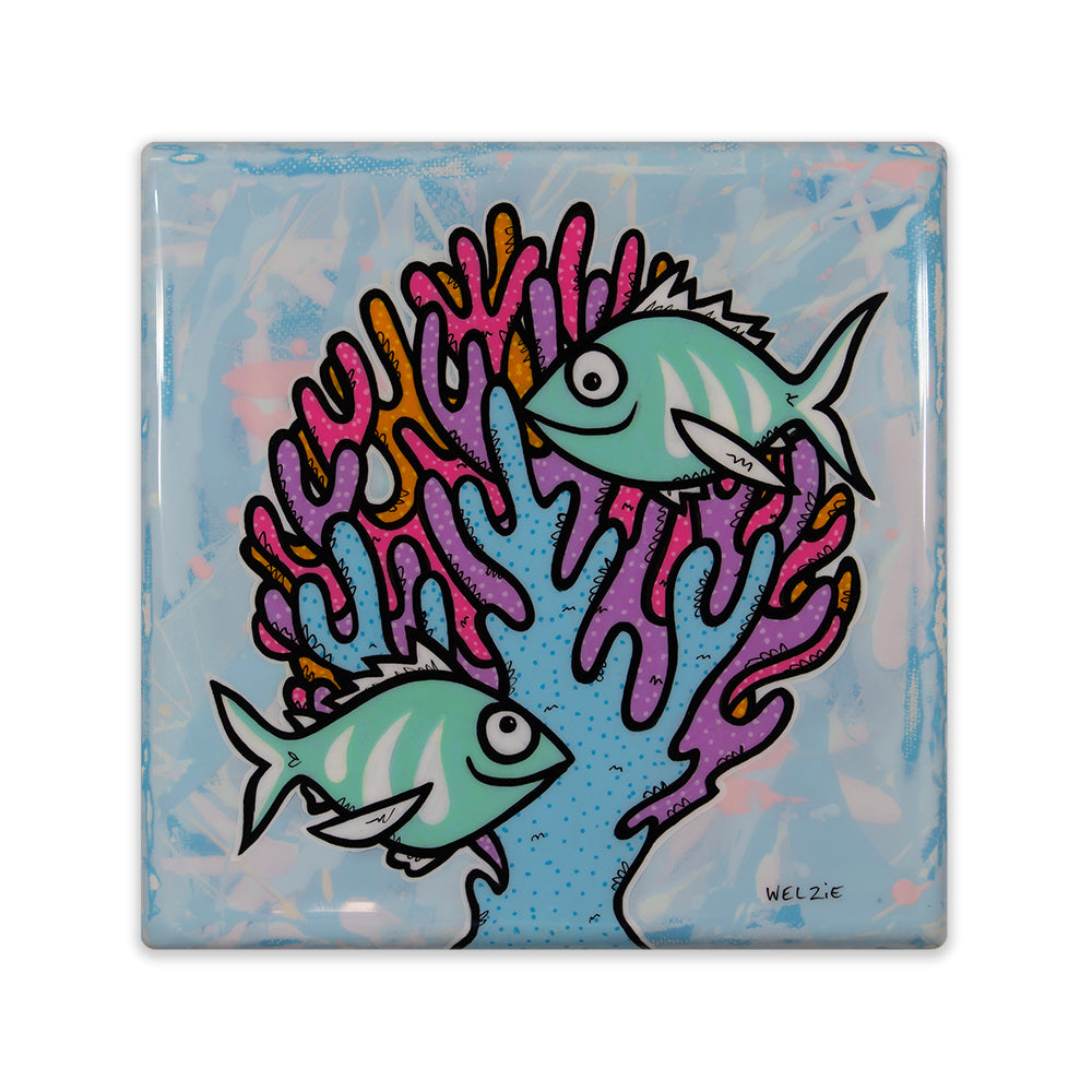 A square art tile featuring a whimsical illustration of two light blue fish swimming among vibrant pink, purple, and orange coral on a textured light blue background. Signed 'WELZIE' in the bottom right corner.