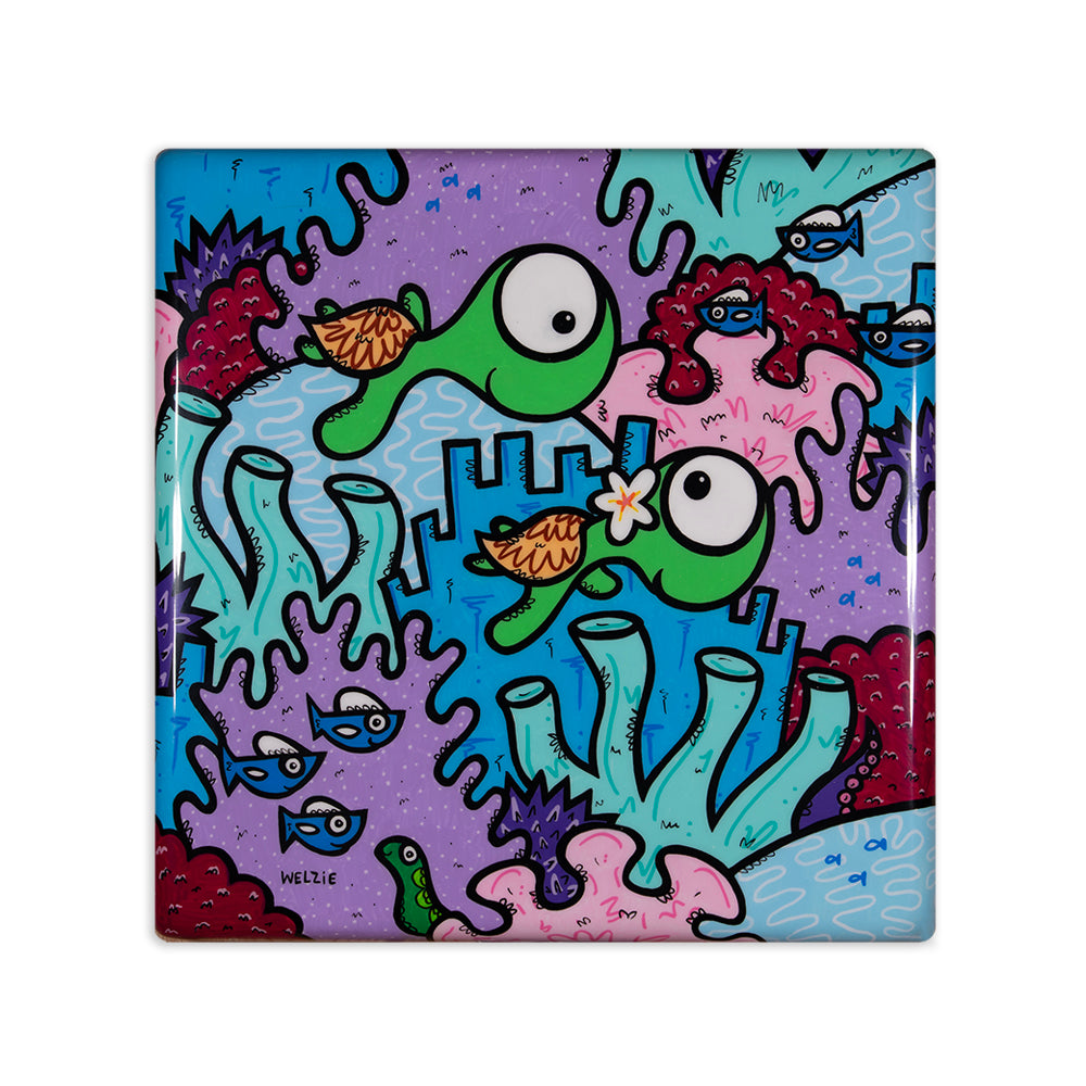 A square ceramic tile coaster featuring a colorful cartoon underwater scene with two green fish, blue fish, and coral in shades of purple, blue, pink, and red. The tile is shown on a clean white background.